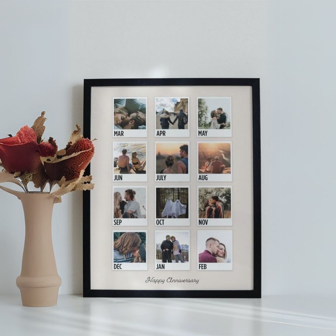 A custom photo collage frame with slots for 12 monthly photos, with a 'Happy Anniversary' message at the bottom, displayed on a white surface next to a vase with dried flowers.