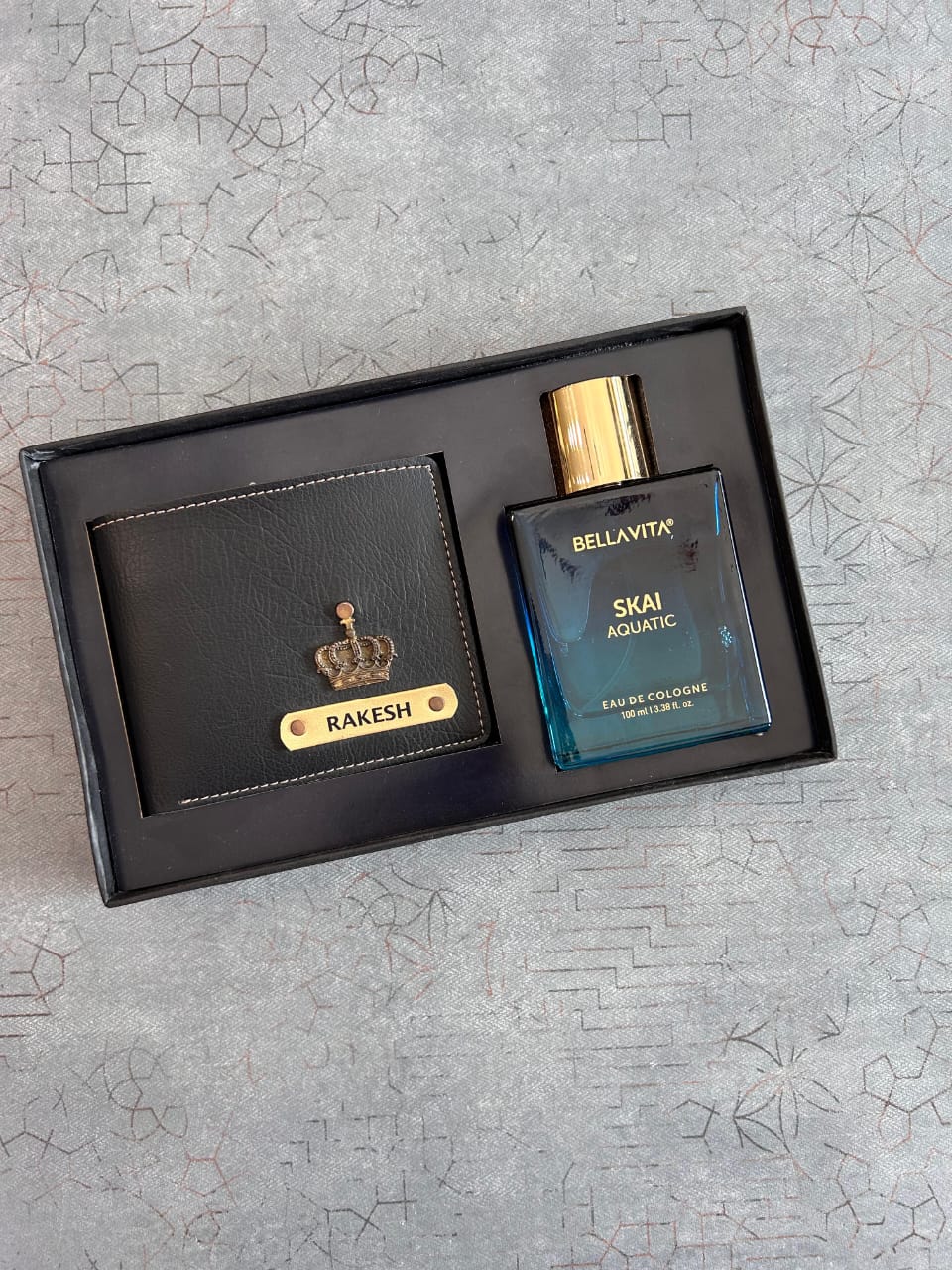 Gift set with black wallet and cologne bottle on a textured gray surface