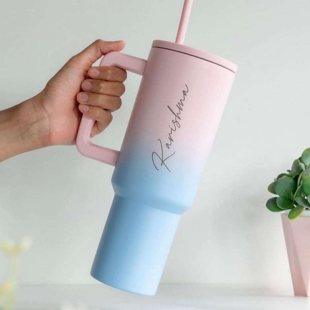 Gradient pink to blue tumbler with straw held by a hand on a light background