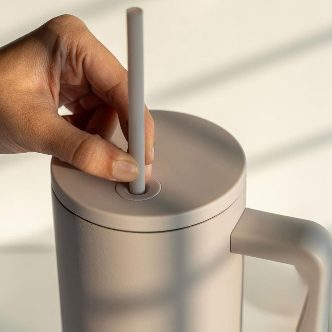 Hand placing a straw into a beige tumbler on a light background