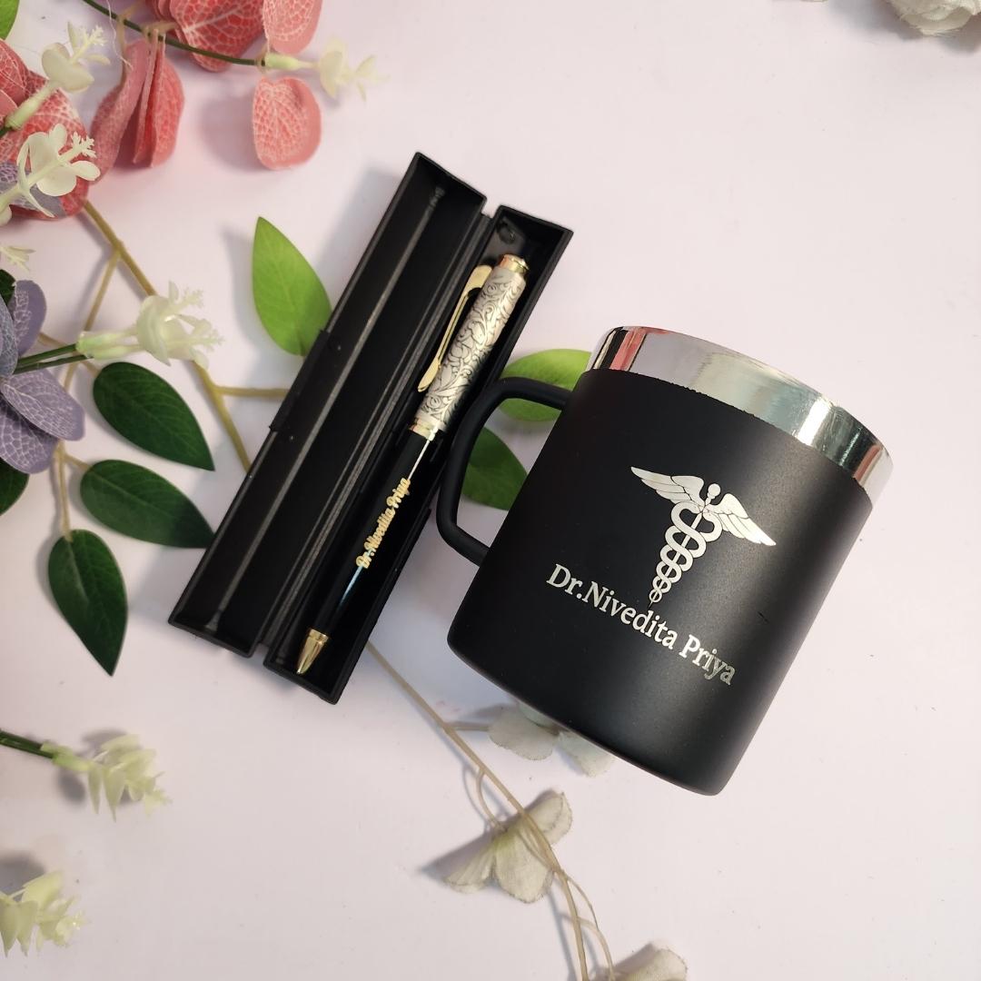 Black mug with silver lid and 'Dr. Nivedita Priva' branding, accompanied by a pen set on a floral background.