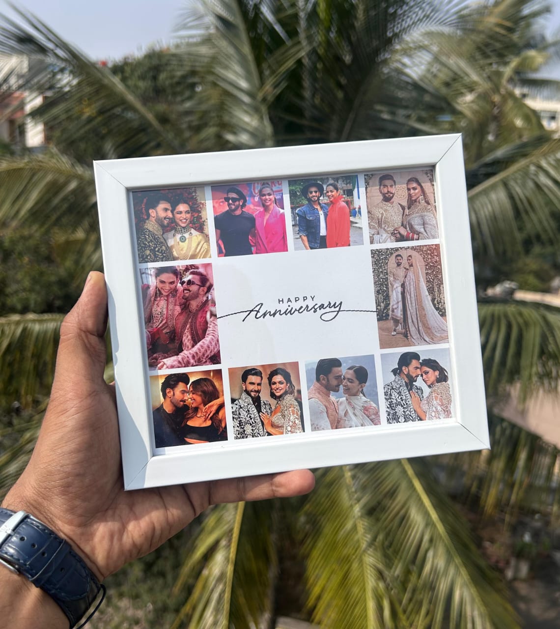 Hand holding a collage photo frame with 'Happy Anniversary' text against a palm tree background