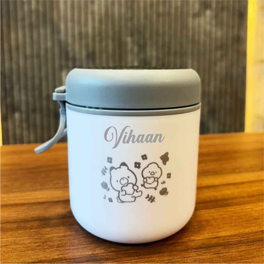 White container with gray lid on a wooden surface, featuring 'Vihaan' branding and cartoon characters.