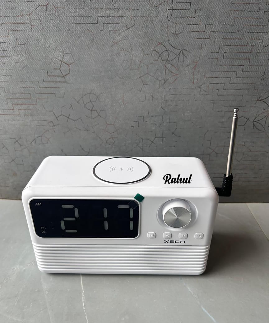 White digital clock radio with 'Rahul' branding on a gray surface and wall.