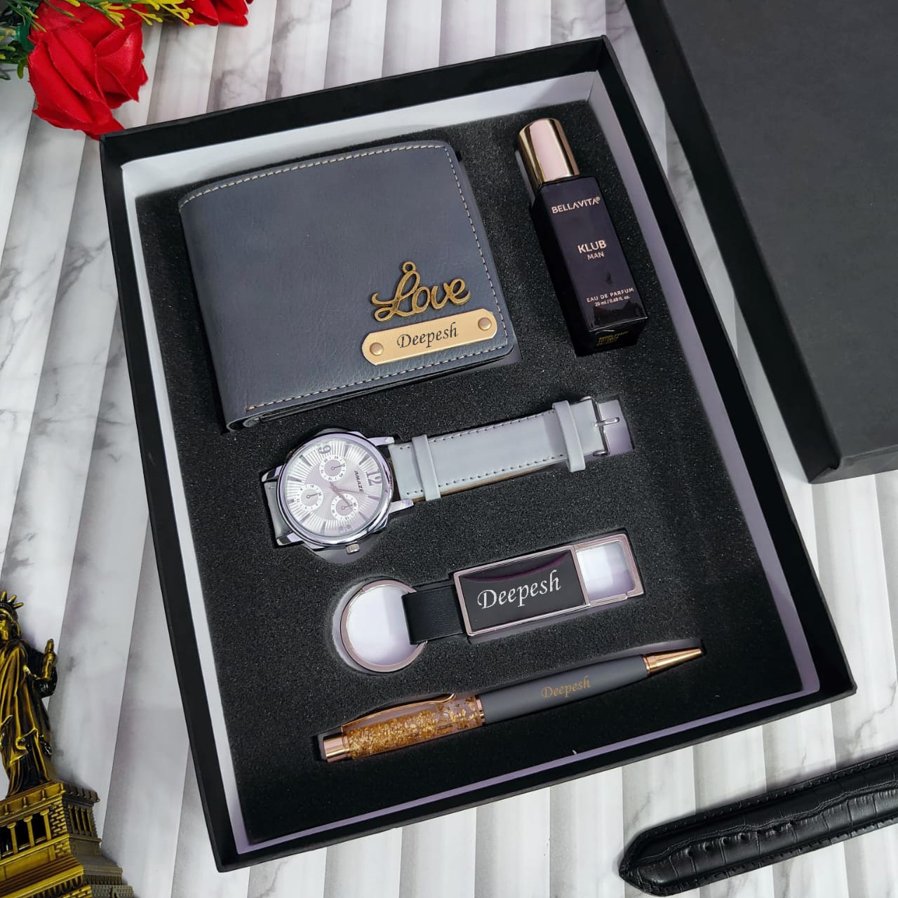 Groomsmen gift set with wallet, watch, pen, and perfume in a box on a marble surface.