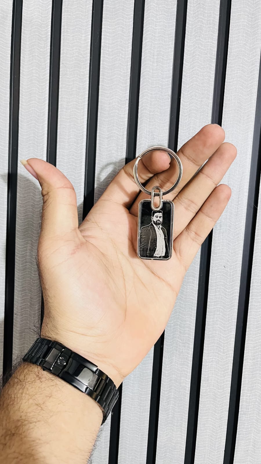 Hand holding a keychain with a small rectangular tag featuring an engraved design against a striped background.