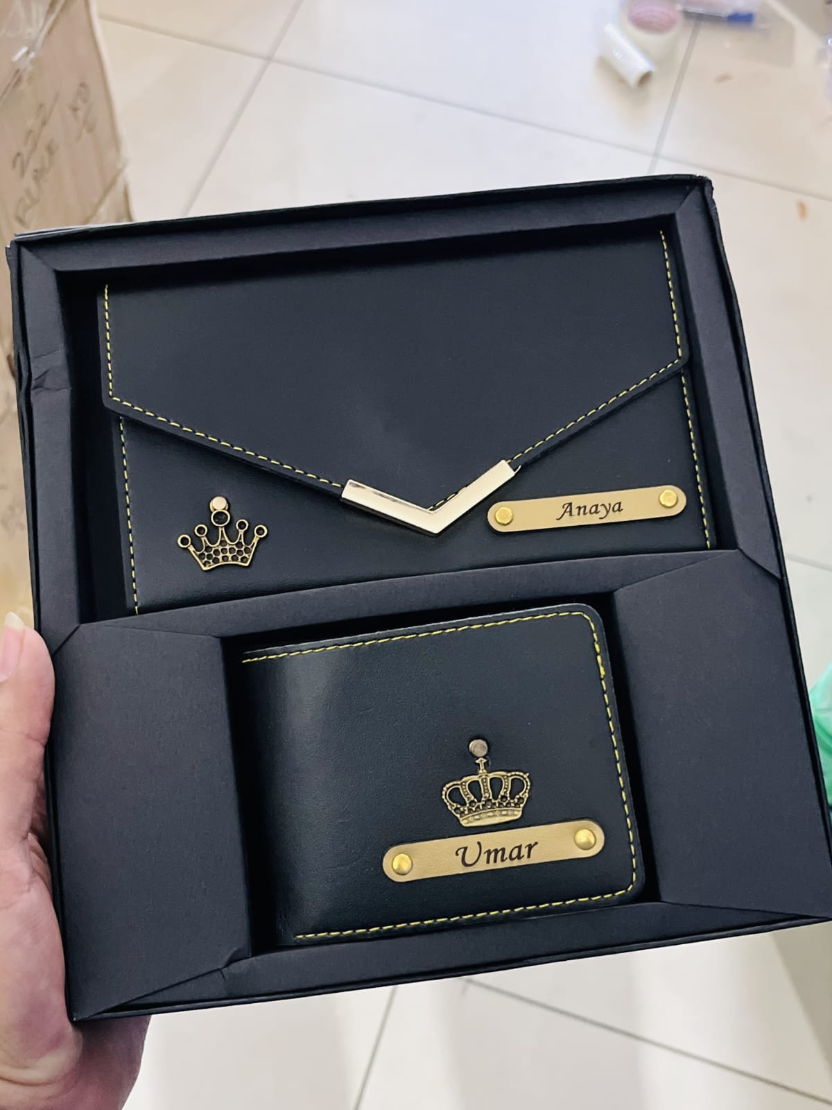 Black leather wallet and cardholder set with gold accents in a box, held by a hand.