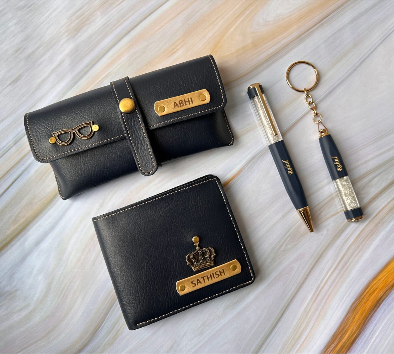 Black wallets, pen, and keychain with personalized names on a light wood surface