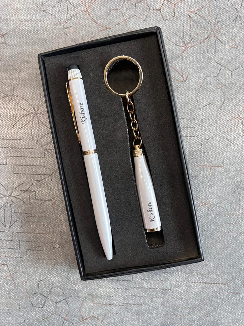 White pen and keychain set with gold accents in a black box on a textured gray surface
