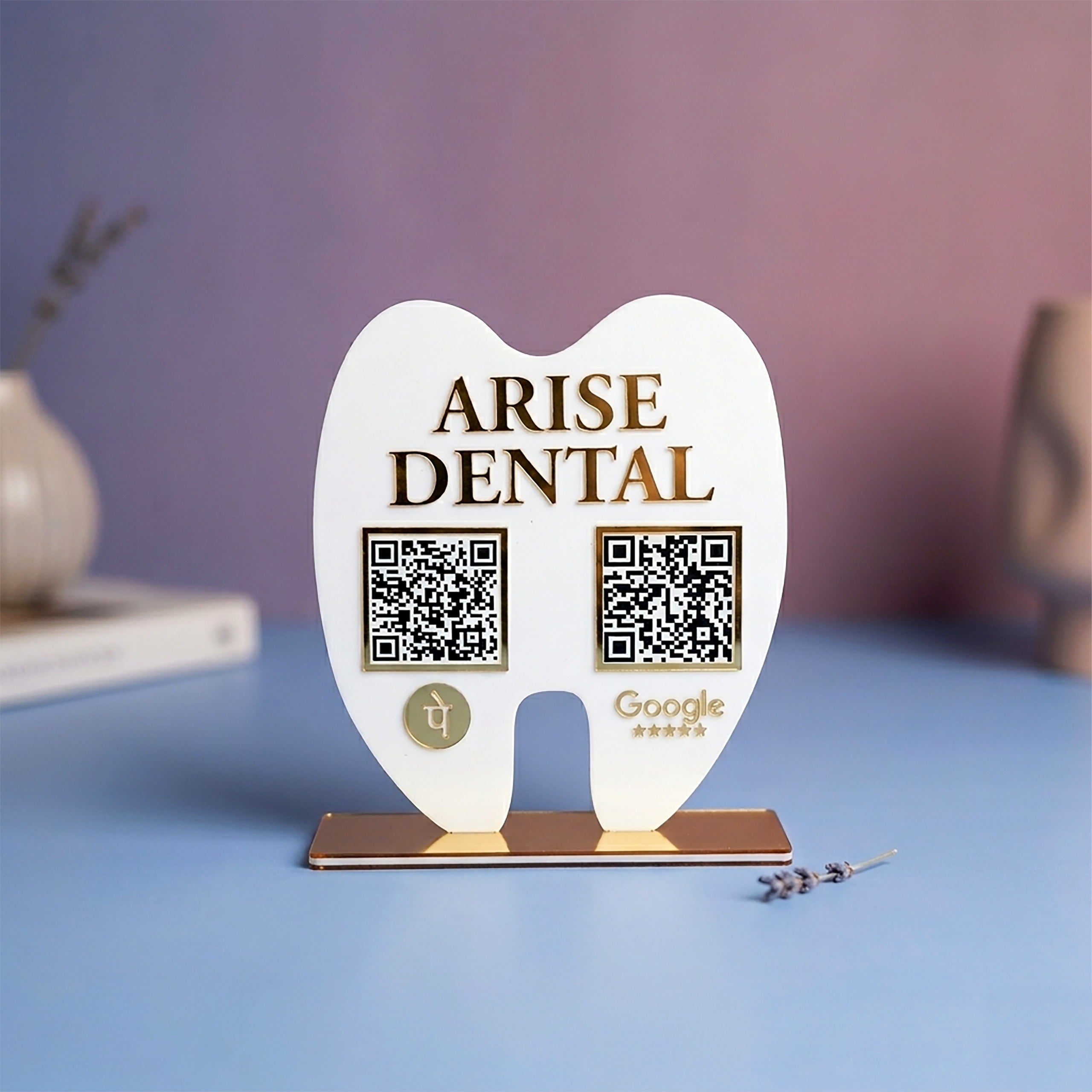 White tooth-shaped stand with 'Arise Dental' branding and QR codes on a blue surface.