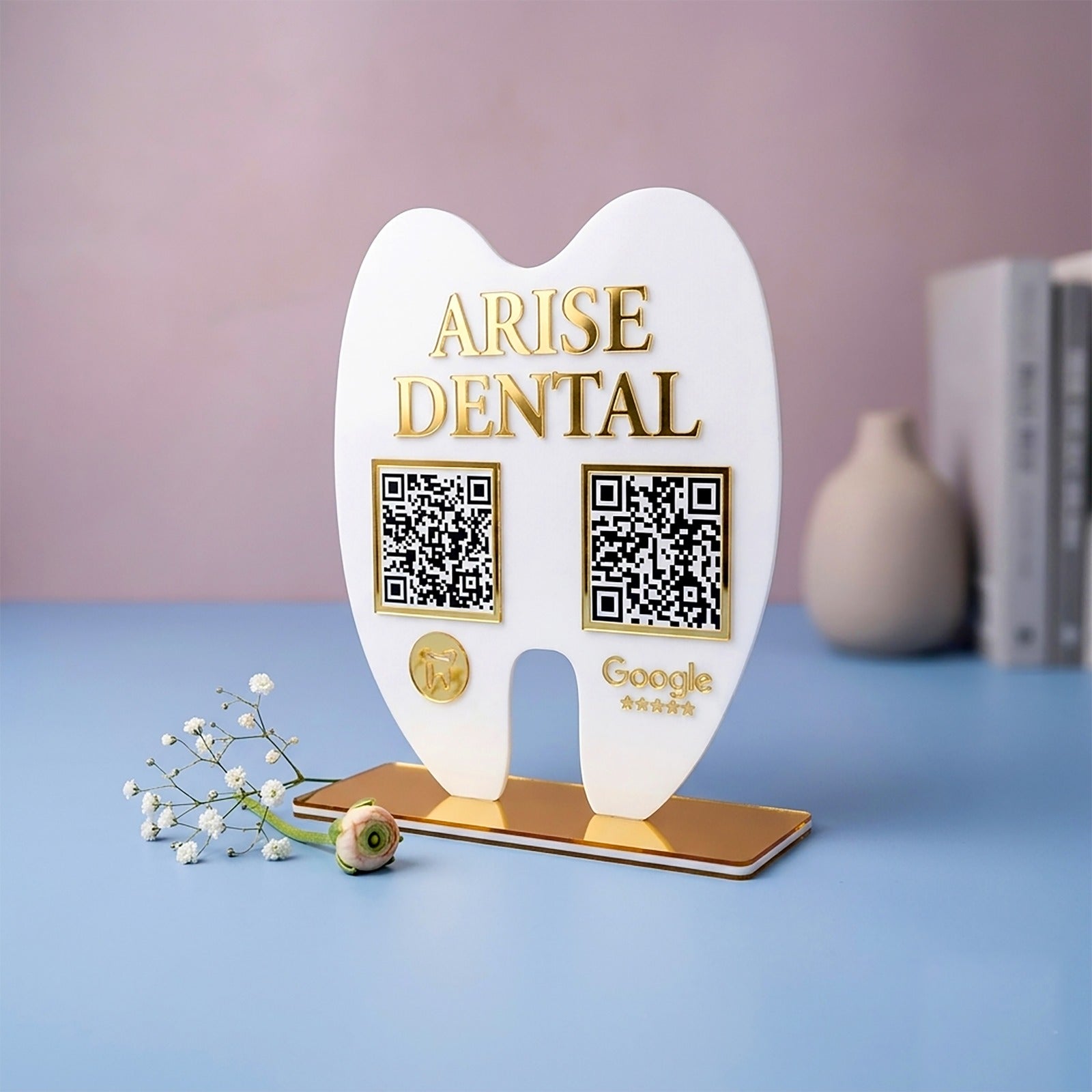 White tooth-shaped stand with 'Arise Dental' branding on a blue surface with a pink background.