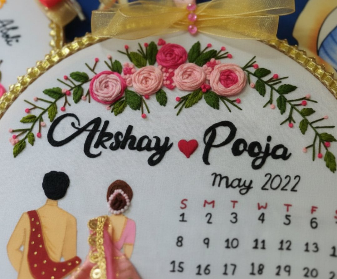 Embroidered hoop with floral design, names 'Akshay' and 'Pooja', heart symbol, and a calendar for May 2022.