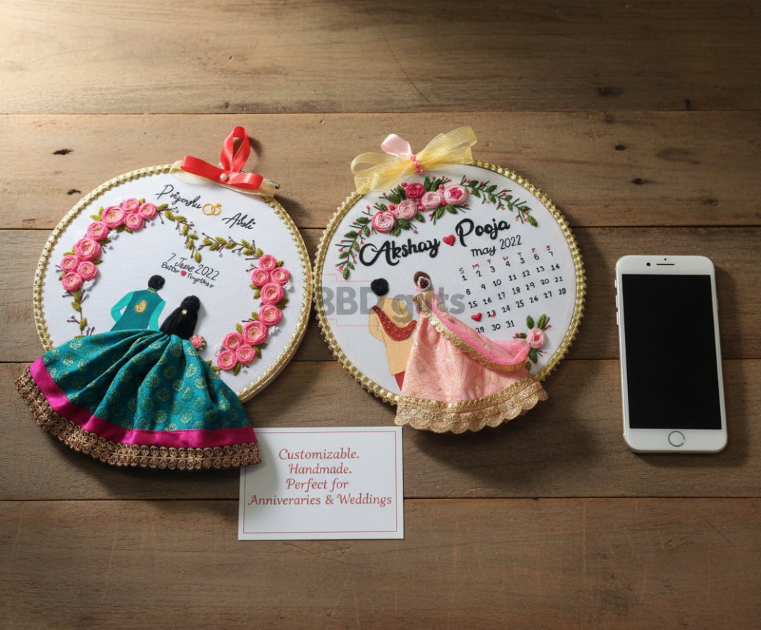 Two embroidered wall hangings with floral designs and text on a wooden surface, next to a smartphone.