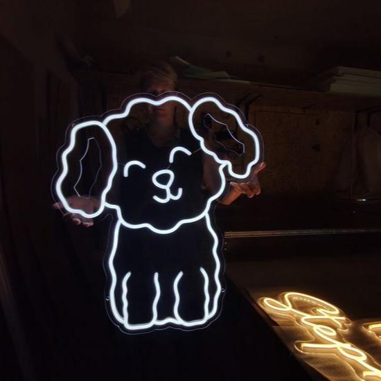 A person holding a neon sign in the shape of a Bichon Frise dog with a 'DOG' sign on its mouth.