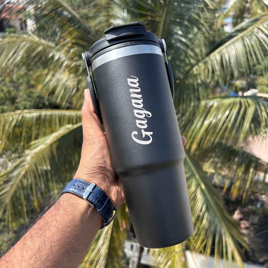 Hand holding a black water bottle with 'Gagana' text against a palm tree background.