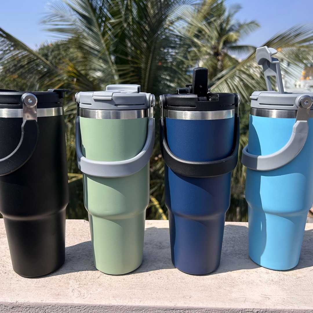 Four insulated tumblers in black, green, blue, and black with palm trees in the background.