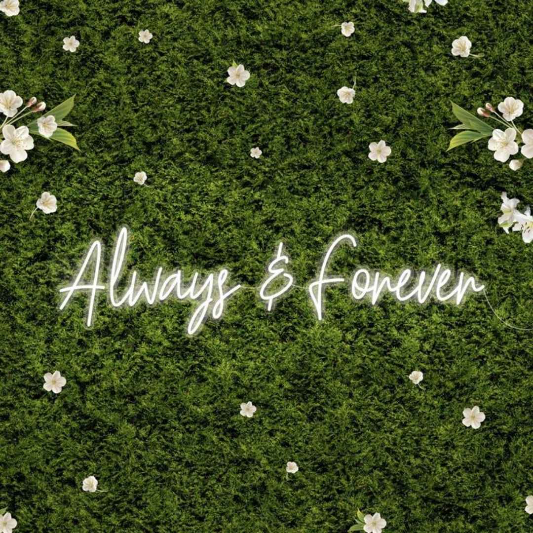 Neon sign with 'Always & Forever' on a green moss background with white flowers