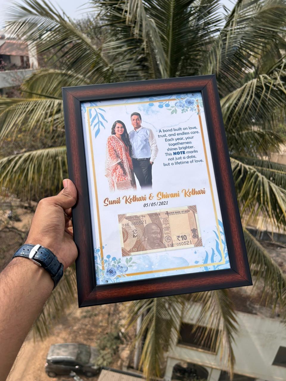 Framed photo of a couple with text and a banknote design, held against a palm tree background.