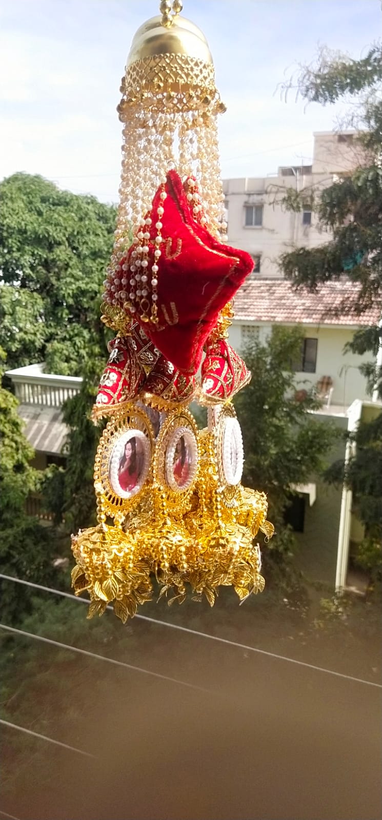 Decorative item with gold and red elements hanging against a blurred outdoor background