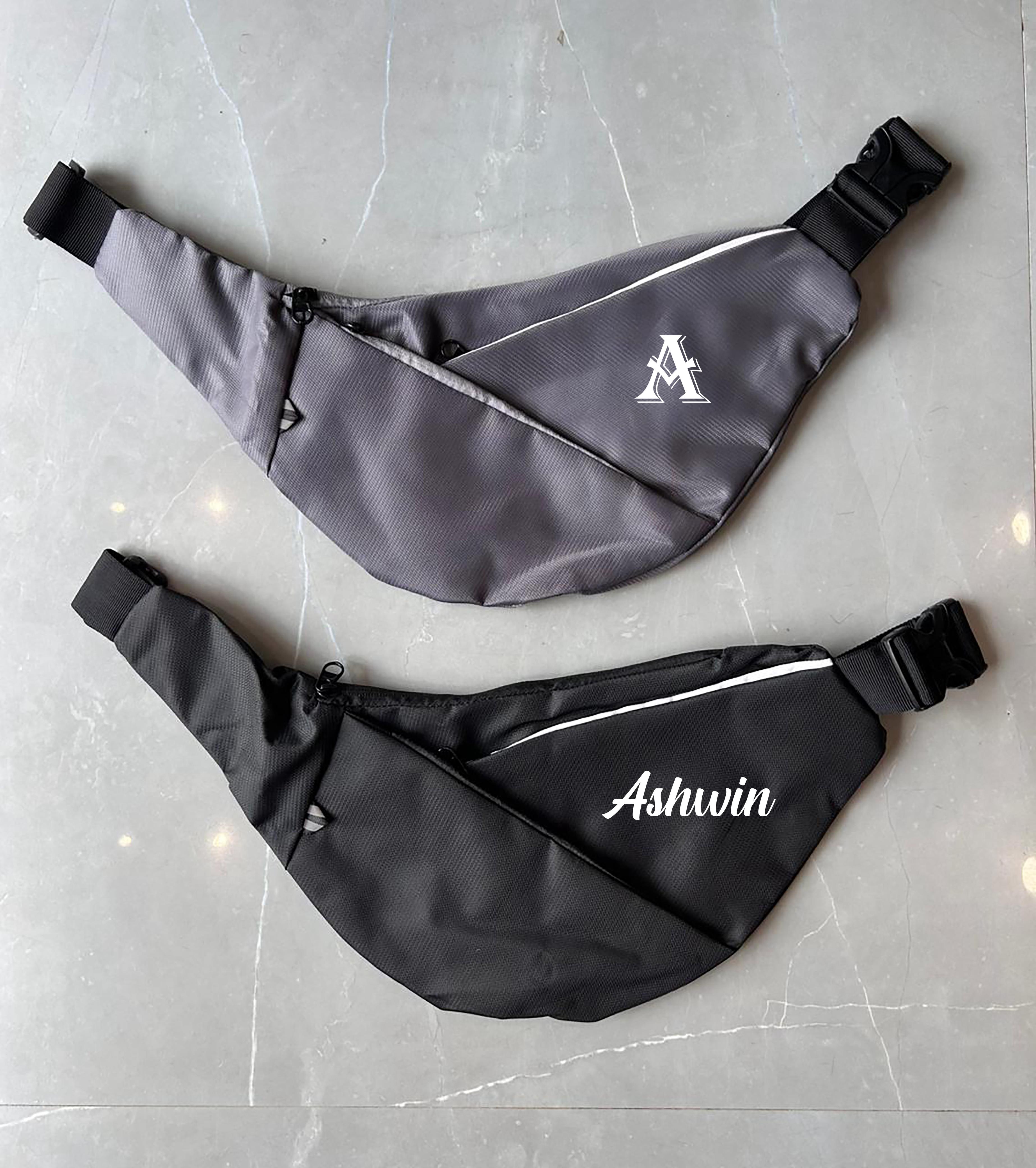 Two fanny packs, one gray and one black with 'Ashwin' branding, on a light gray surface.