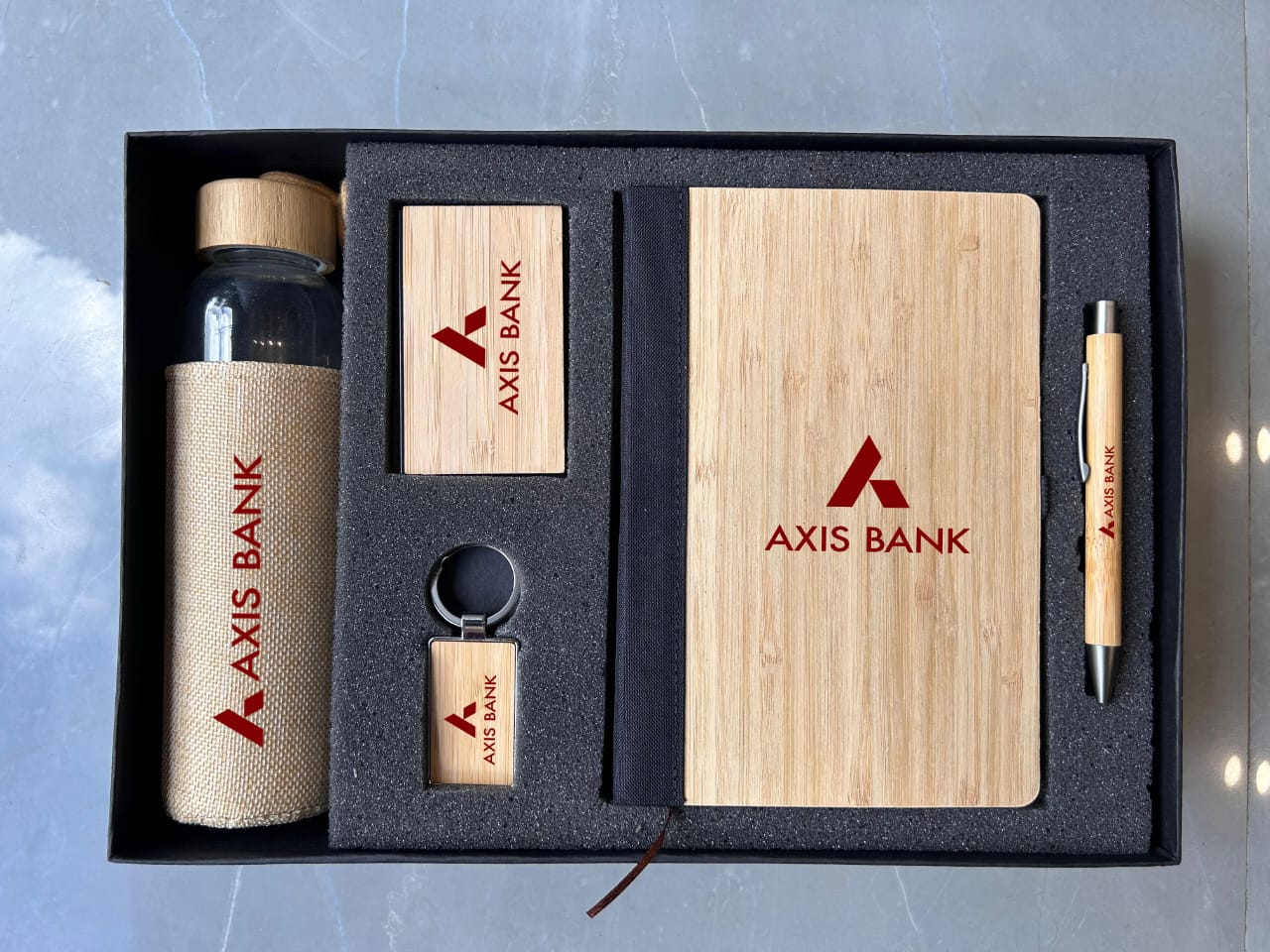Set of Axis Bank branded stationery items including a notebook, pen, and bottle on a gray background