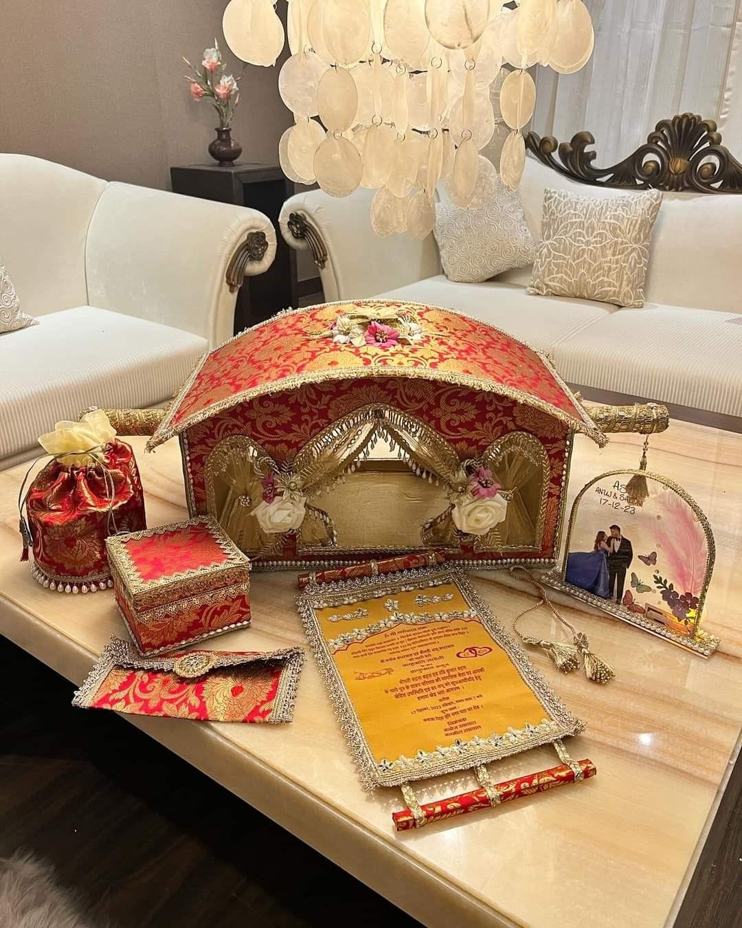 Decorative items including a jewelry box, cards, and a photo frame on a table with a sofa and chandelier in the background.