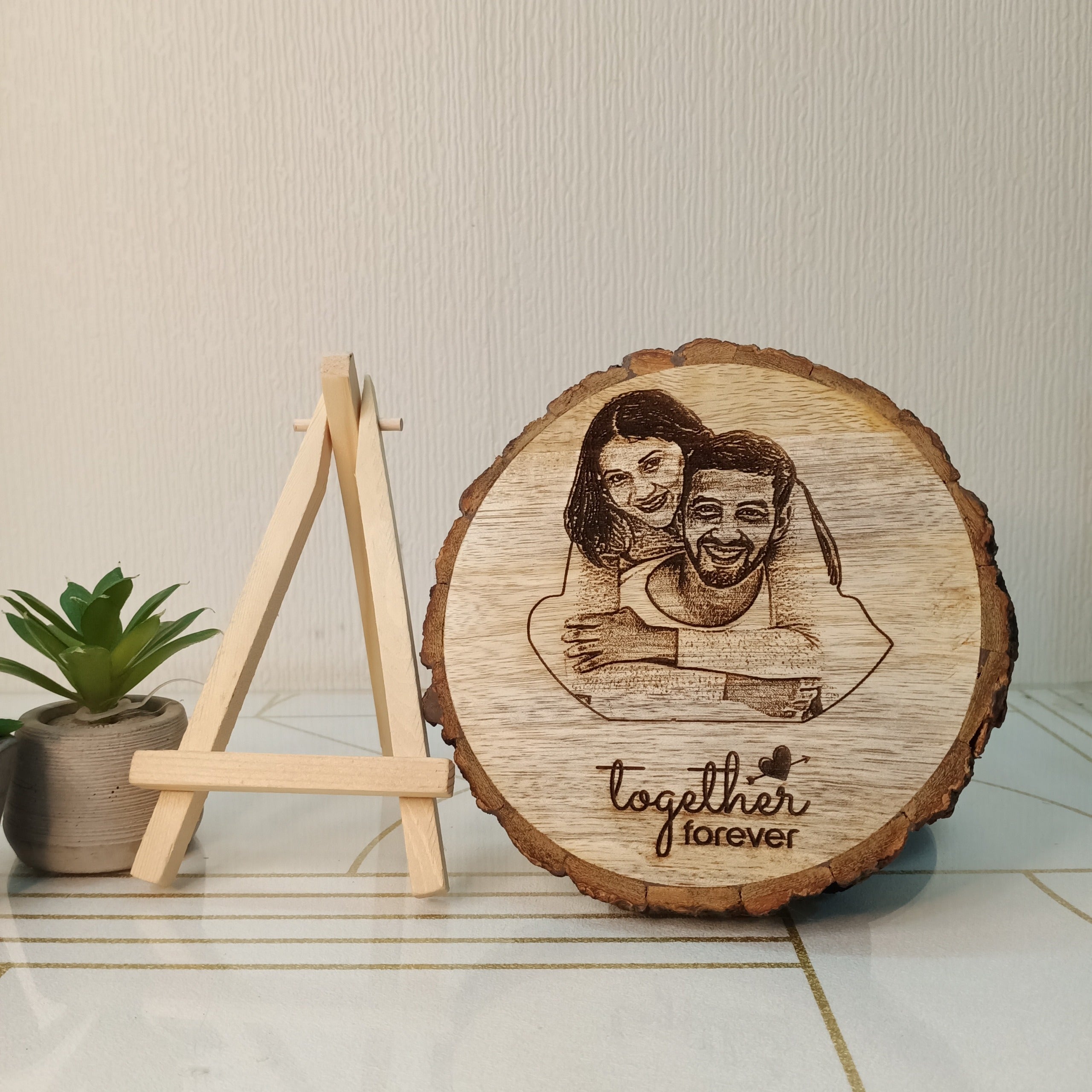 Wooden plaque with engraved couple and 'together forever' text, placed on a surface with a plant in the background.