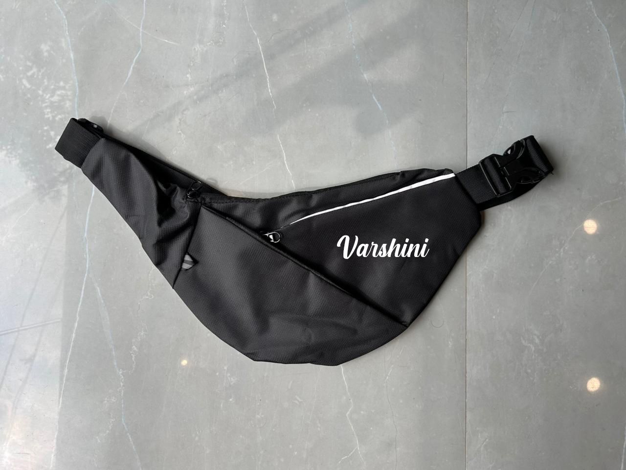 Black waist bag with 'Varshini' branding on a gray surface