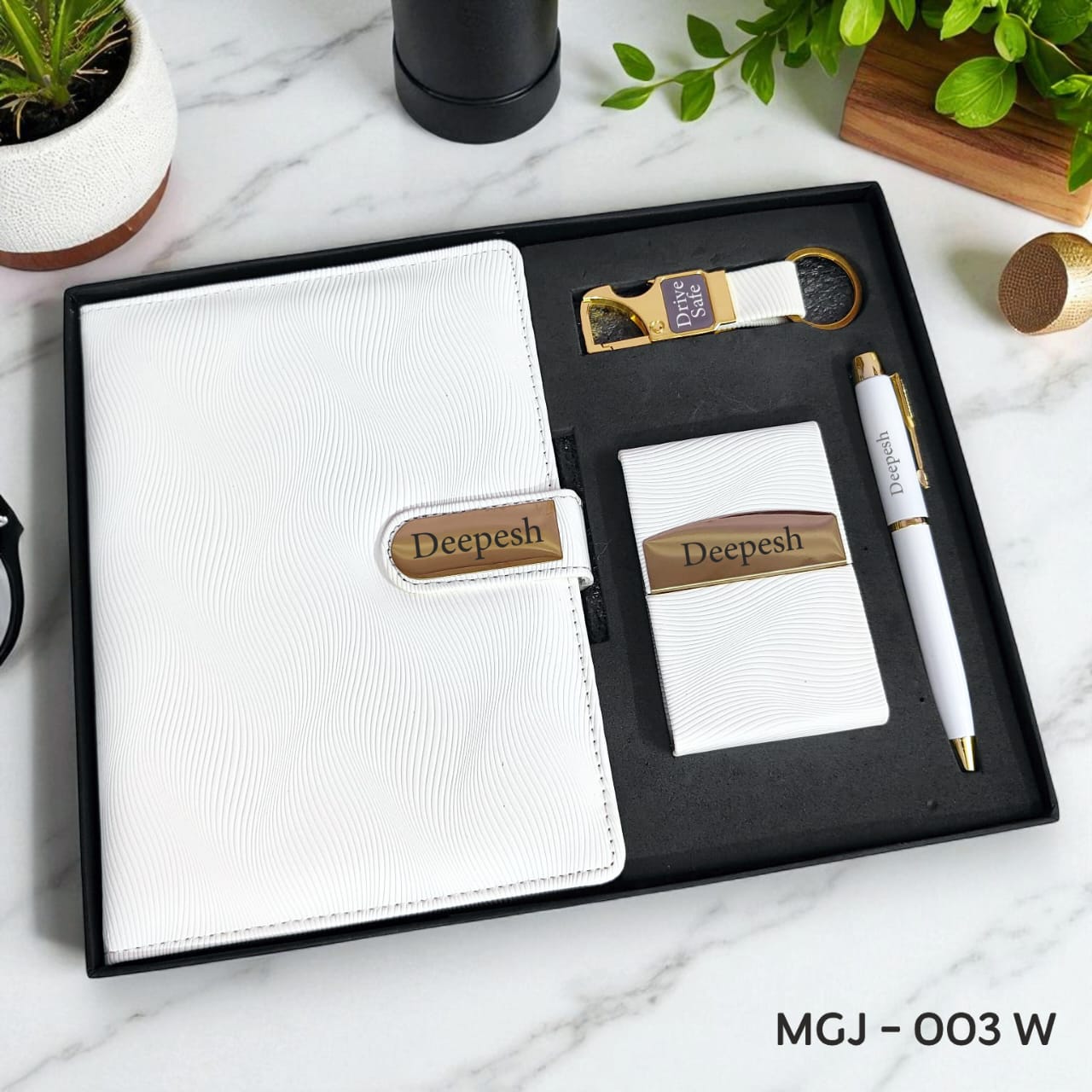 Gift set with white notebook, pen, and other items in a black box on a marble surface.