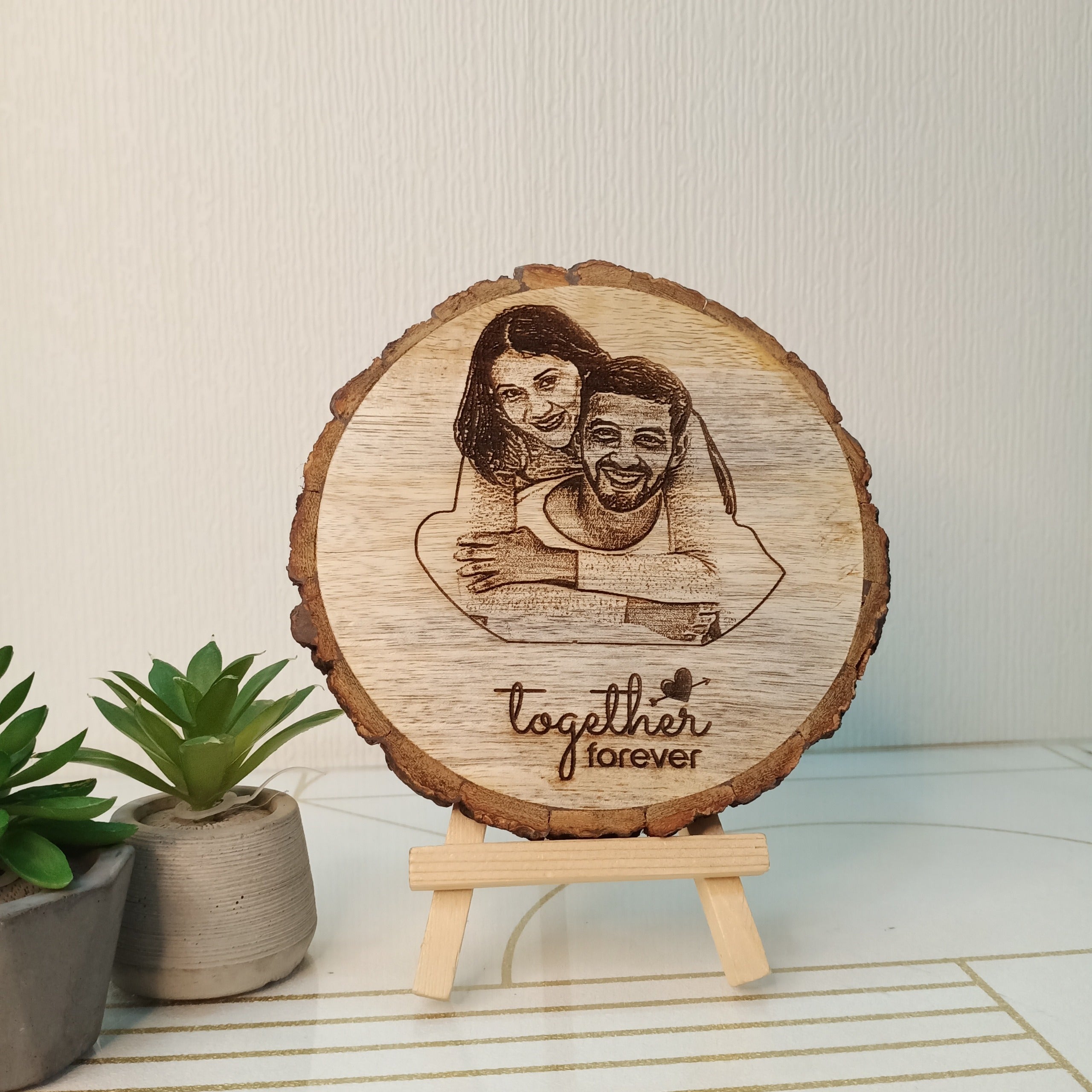 Wooden plaque with engraved couple and 'Together Forever' text, placed on a stand with plants in the background.
