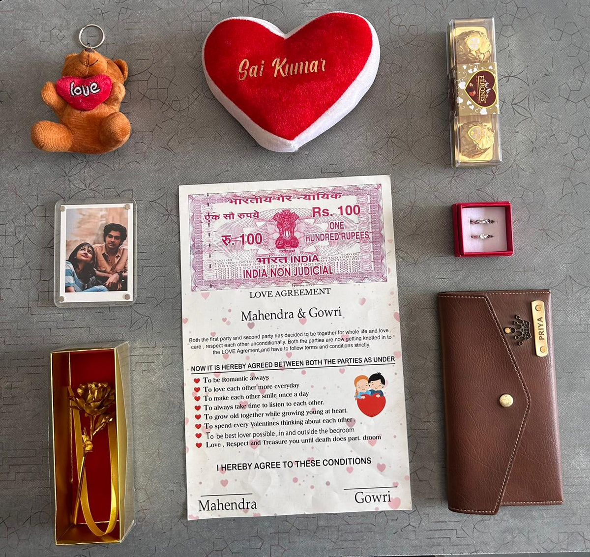 Collection of romantic items including a heart-shaped pillow, teddy bear, and 'love agreement' paper on a gray surface.