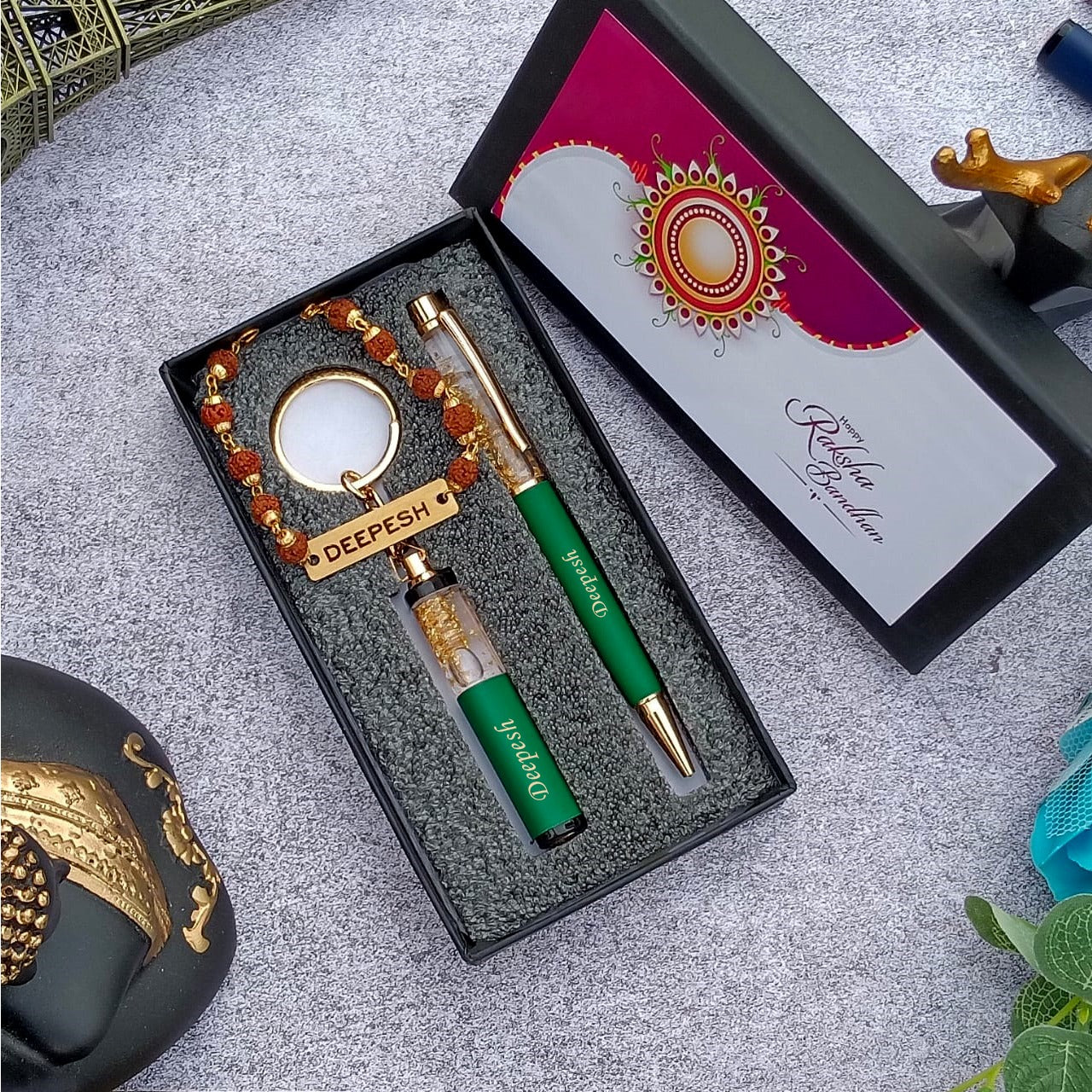 Brother gift combo in box there is one customized green pen and cutkey chain highquality rudraksh rakhi with name, beside box cap is there where greeting are written on it 