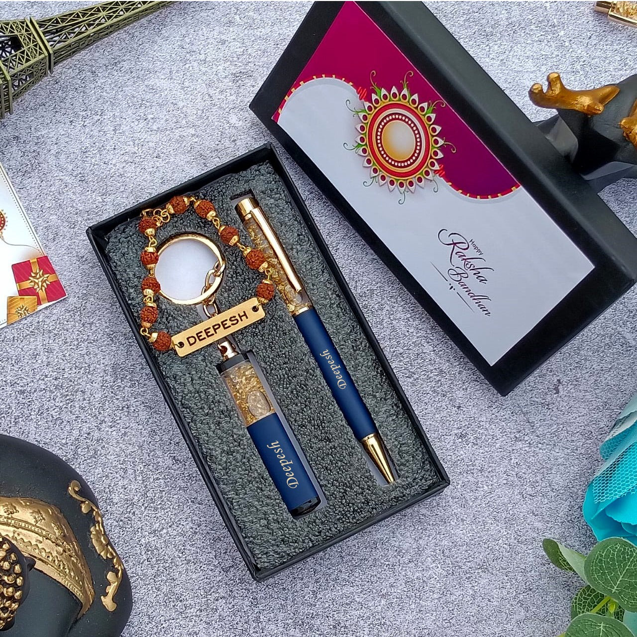 Brother gift combo in box there is one customized blue pen and cutkey chain highquality rudraksh rakhi with name, beside box cap is there where greeting are written on it 