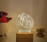 A heart-themed decorative lamp with an anatomical heart illustration, a heart rate line, and the custom text  displayed prominently. The lamp emits a warm glow from a wooden base, creating a cozy ambiance. The model number "Model -1" is written above the design.