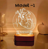 A heart-themed decorative lamp with an anatomical heart illustration, a heart rate line, and the custom text  displayed prominently. The lamp emits a warm glow from a wooden base, creating a cozy ambiance. The model number "Model -1" is written above the design.