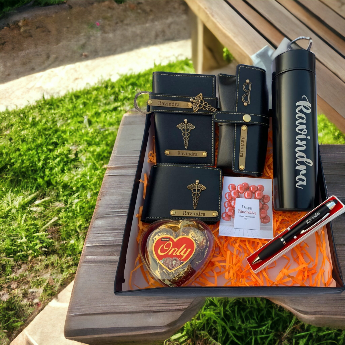 customized hamper for doctor, placed on table ,7 itmes are there black mens wallet and passport cover and spets cover and temparature bottle ,black pen with customized named and having one chocolate box 