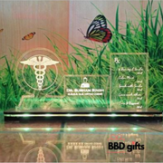 The image shows a personalized glass desk nameplate for Dr. Subham Singh, M.B.B.S., M.S., M.D. Ortho (AIMS). The nameplate includes the medical caduceus symbol on the left, the doctor's name and qualifications in the center, and a list of motivational prescriptions on the right, such as 