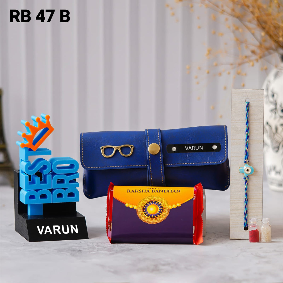 Best Bro 3D pen stand, personalized eyewear case with custom name and charm, Kit-Kat chocolate, Rakhi, and Roli Chawal. placed in floor background some flower vessale there