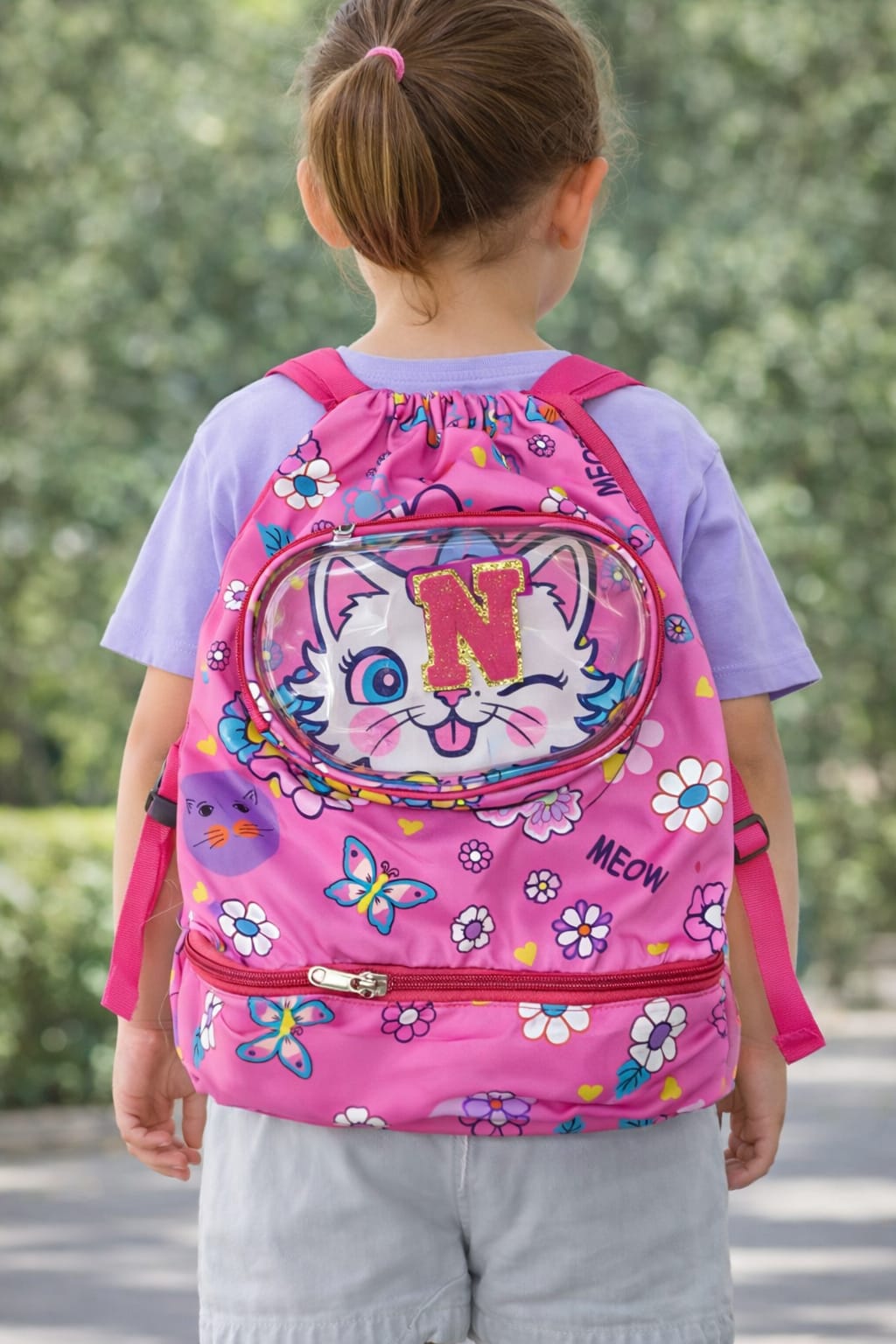 Child wearing a pink backpack with a cartoon cat design outdoors.