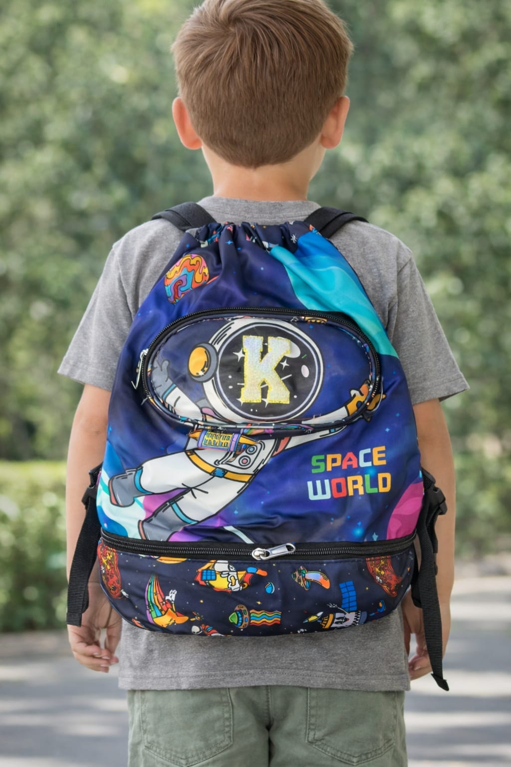 Child wearing a colorful backpack with space-themed design outdoors.