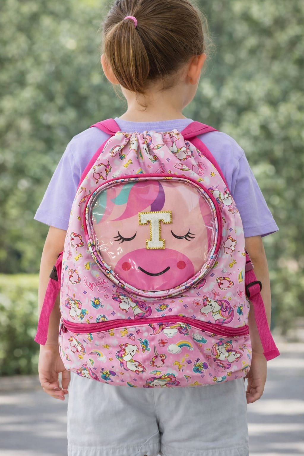 Child wearing a pink backpack with a cartoon face design outdoors.