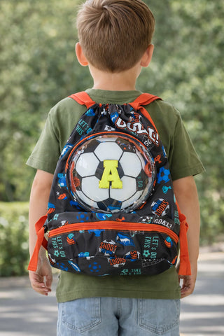 Child wearing a backpack with a soccer ball design outdoors