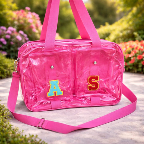Pink clear handbag with colorful letters 'A' and 'S' on a blurred natural background