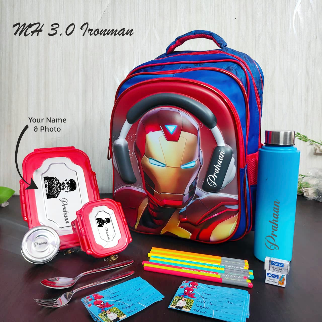 Backpack with Ironman design, lunch box, water bottle, and stationery items on a table.