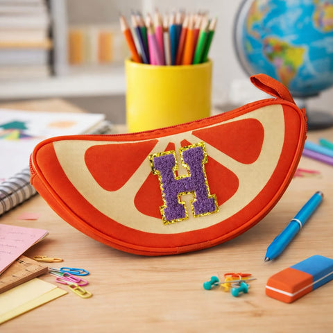 Pencil case shaped like a watermelon slice with 'HP' on a desk with stationery items