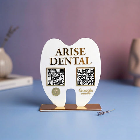 White tooth-shaped stand with 'Arise Dental' branding and QR codes on a blue surface.