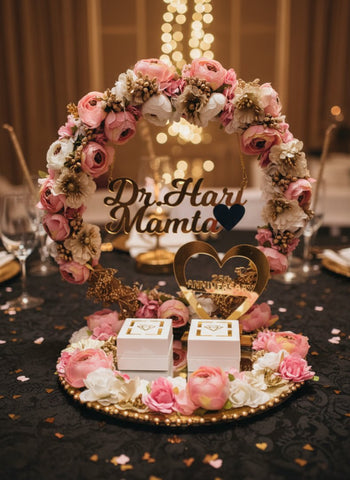 Decorative floral wreath with 'Dr. Hari Mamta' on a table with wine glasses and a blurred background.