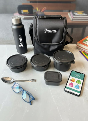 Black lunch bag, containers, bottle, and phone with app on a white surface.