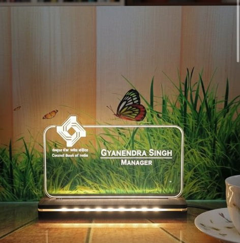 Glass display case with a butterfly on a wooden table, smartphone, and cup in the background.