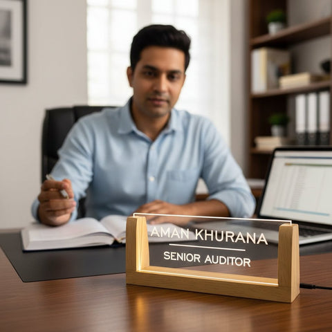 Man sitting at a desk with a nameplate displaying 'Aman Khurana, Senior Auditor' in an office setting.
